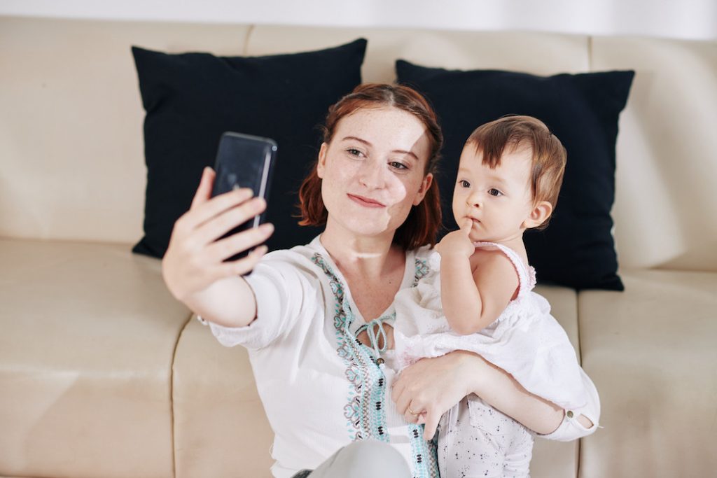 Happy smiling young woman taking selfie with cute little baby daughter
