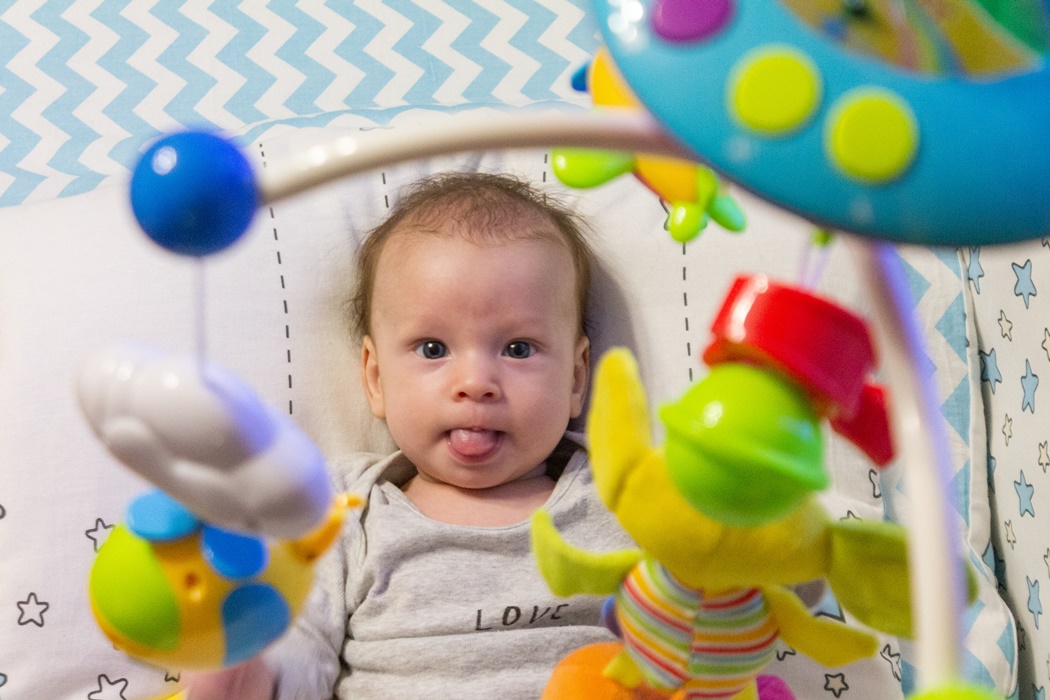 little happy motivated child is playing with dangling rattles, toys for newborn, first toy
