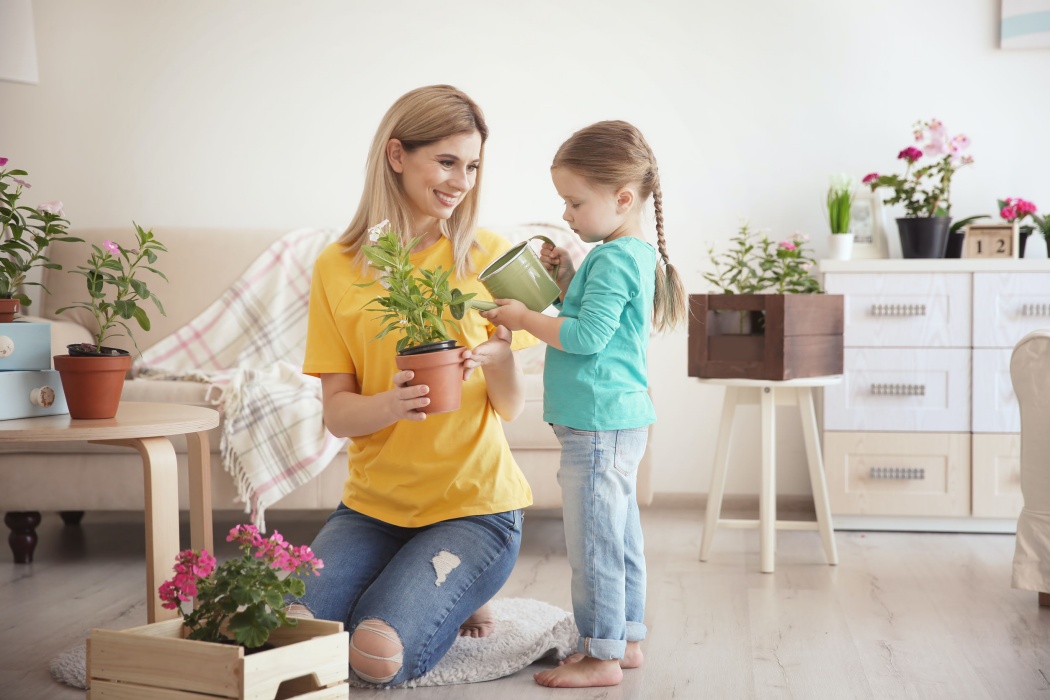 Cute little girl with mother taking care of plants indoors