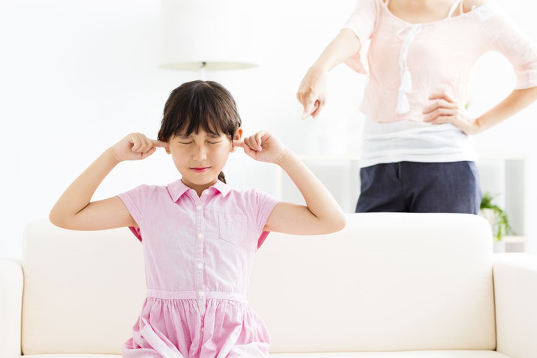 Upset little girl covering her ears while her mother angry