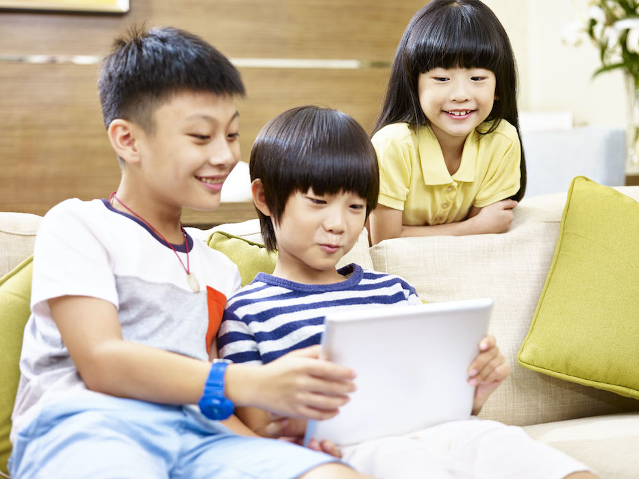 three asian children two little boy and one little girl sitting on couch at home playing video game with digital tablet, focus on the little girl in the back.