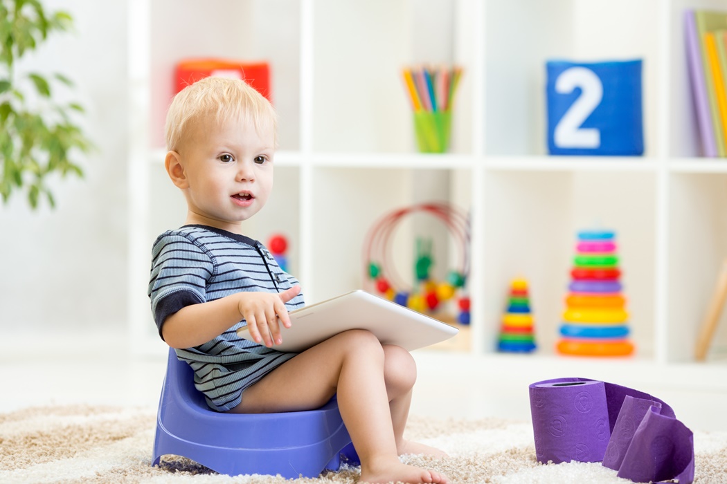toddler sitting on chamber pot playing tablet pc