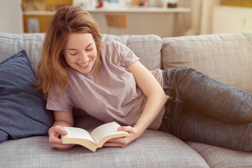 Happy Girl Resting on Sofa While Reading a Book