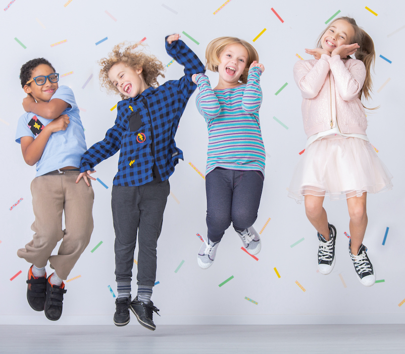 Happy multicultural group of kids jumping against colorful wallpaper