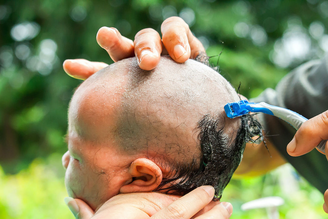 baby girl shaving hair with sharp razor. shaving hair for 1 month baby is traditional in Thailand althought there is a risk to injury.