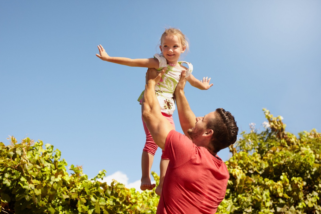 Little girl pretending to be a airplane as her father lifts her in the air. Father holding his daughter up high against sky.