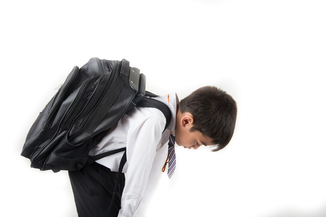 Little school boy taking heavy bag full of books on his back
