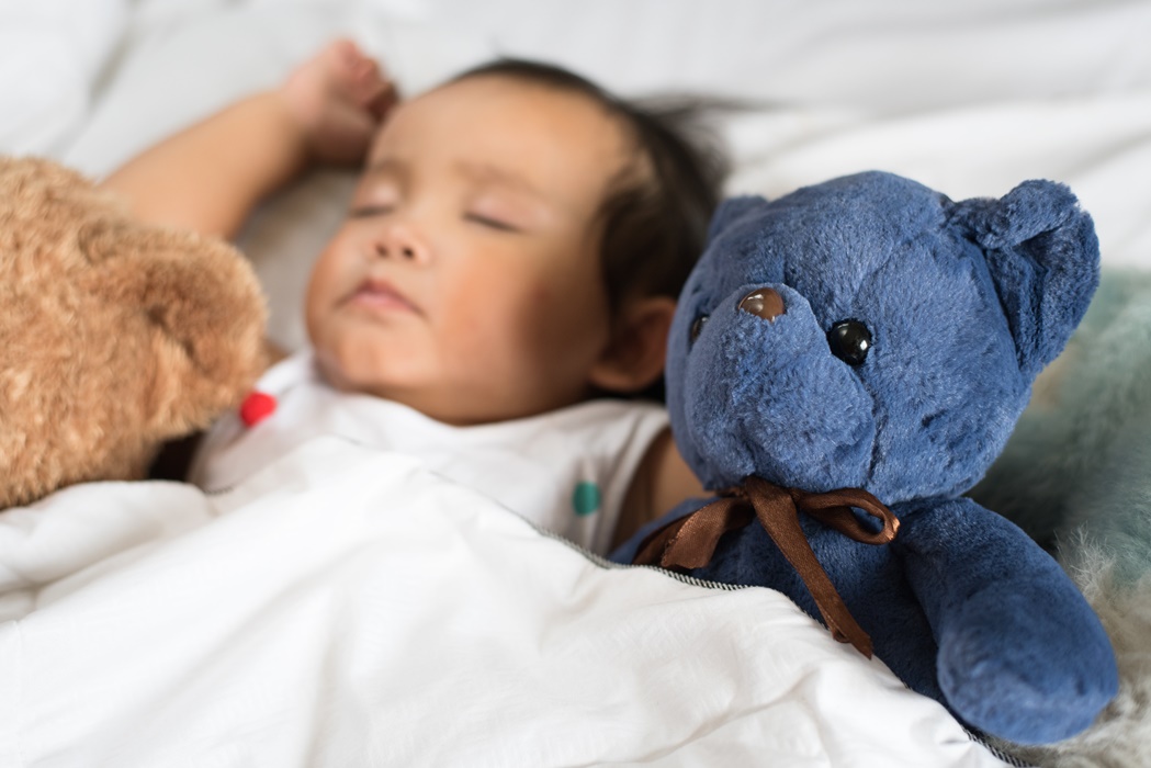 asian toddler sleeping with teddy bear on white bed, pillow and sheet