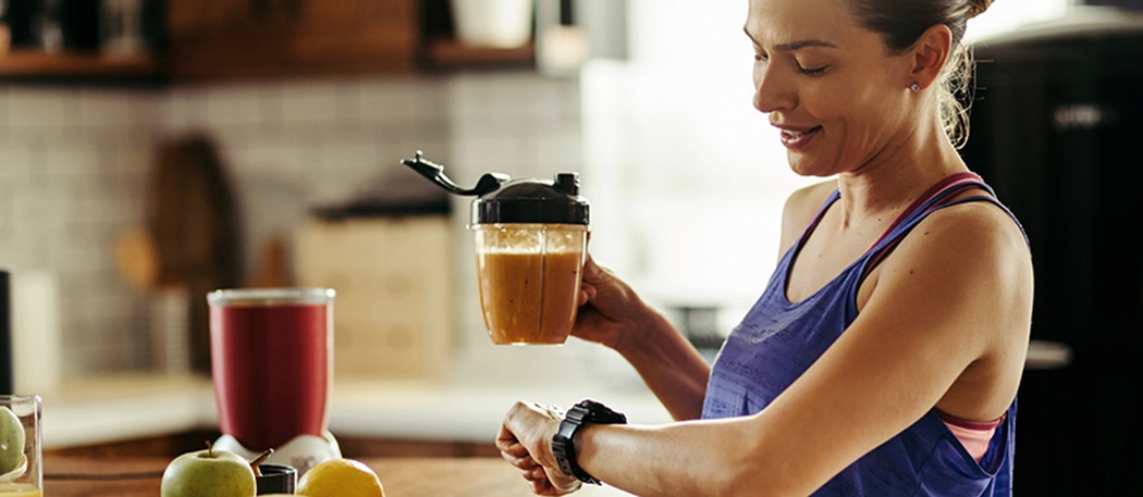 Smiling athletic woman drinking healthy smoothie and checking the time on her wristwatch in the kitchen.; Shutterstock ID 1449981740; Other: ; Purchase Order: 123; Client/Licensee: ; Job: