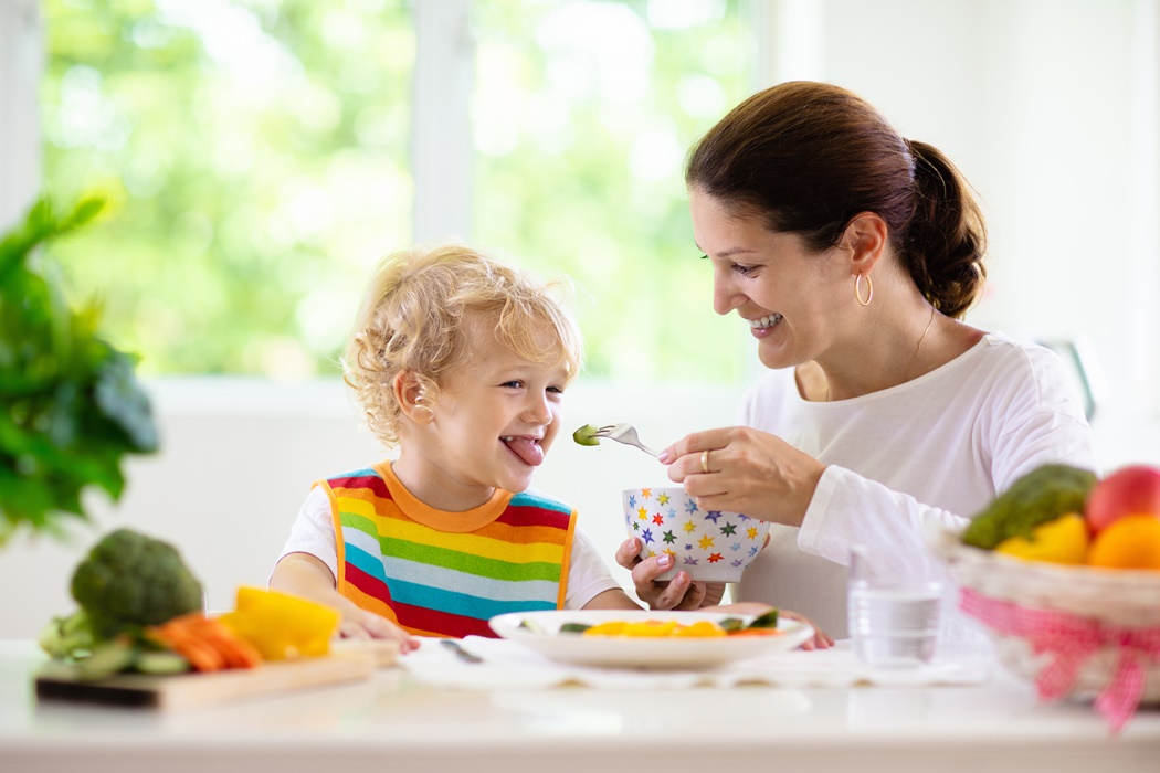 Mother feeding child. Mom feeds kid vegetables