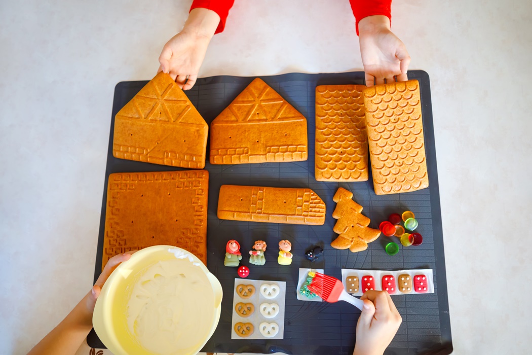 Parts of gingerbread house prepared for baking and decorating. Christmas traditional activity and sweet cake. Active fun for family and kids. Close-up of details. With hands of kids.