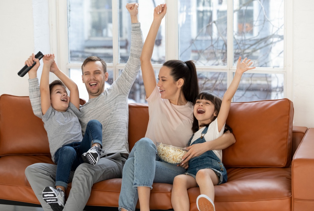 Overjoyed excited family football fans watching sport tv celebrating goal, happy euphoric parents and cute little children kids screaming supporting favorite soccer team victory at home sit on sofa