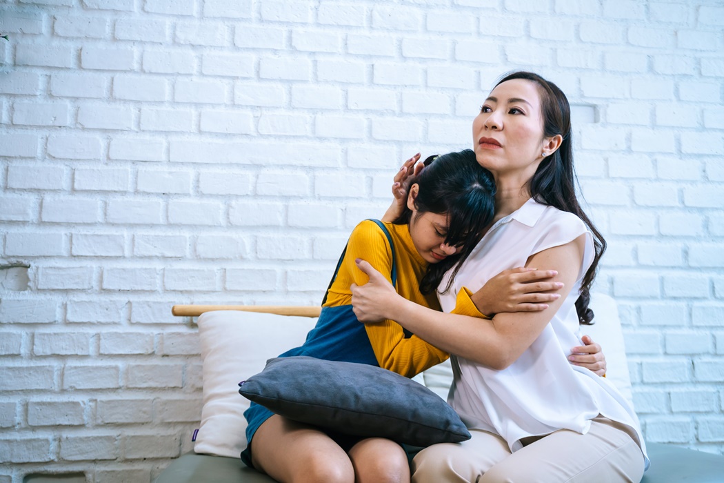 Asian mother comforting crying teenage daughter in miserable, stressed, depressed, sad state of mind