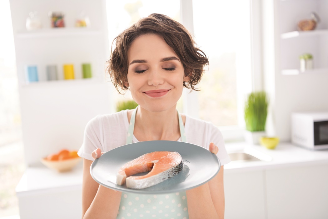 Close up photo of beautiful housewife lady enjoy pleasant smell of fresh raw salmon fillet steak tasty diet breakfast eyes closed hungry wear apron t-shirt stand modern kitchen indoors