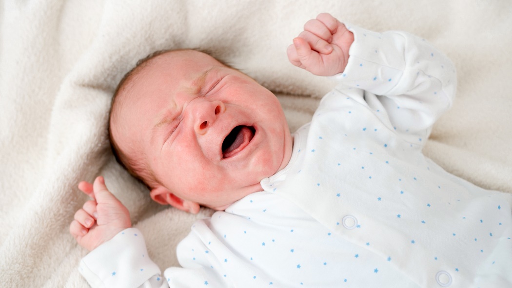 Portrait of little 2 weeks old baby boy crying in baby crib or bed