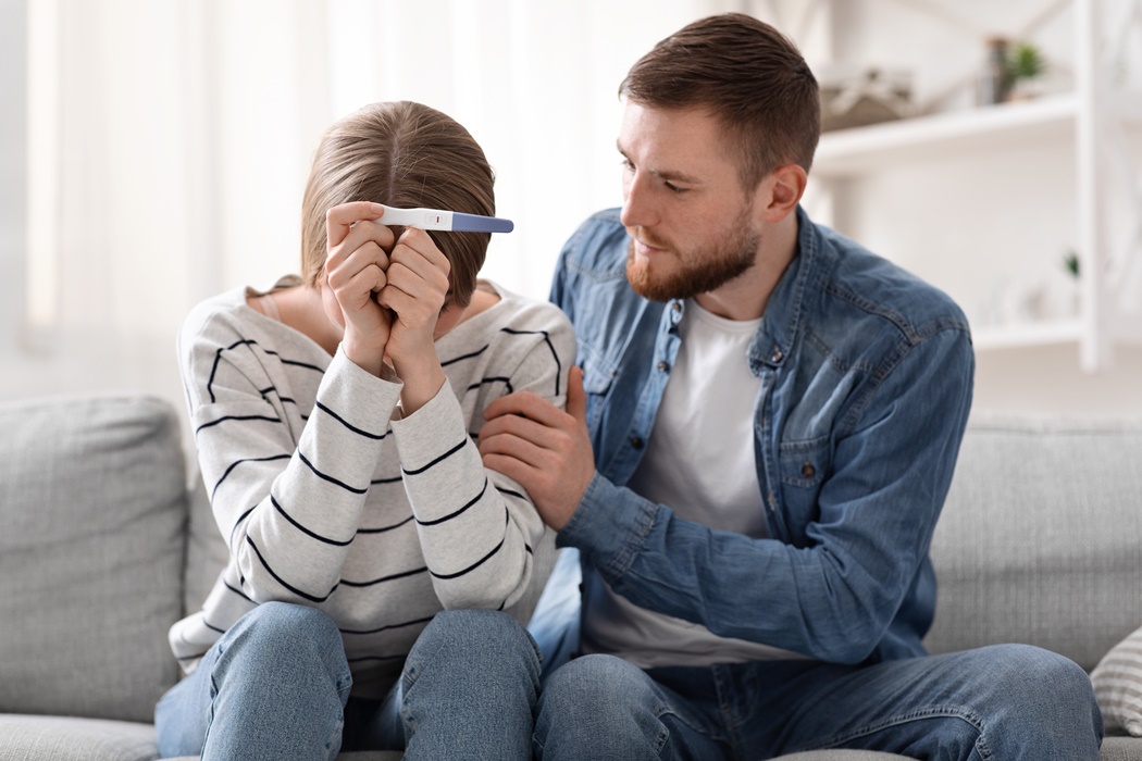 Upset couple sitting with negative pregnancy test result
