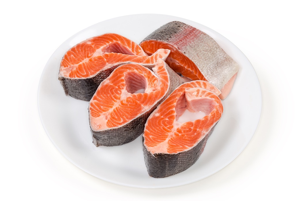 Uncooked steaks of rainbow trout on dish on white background