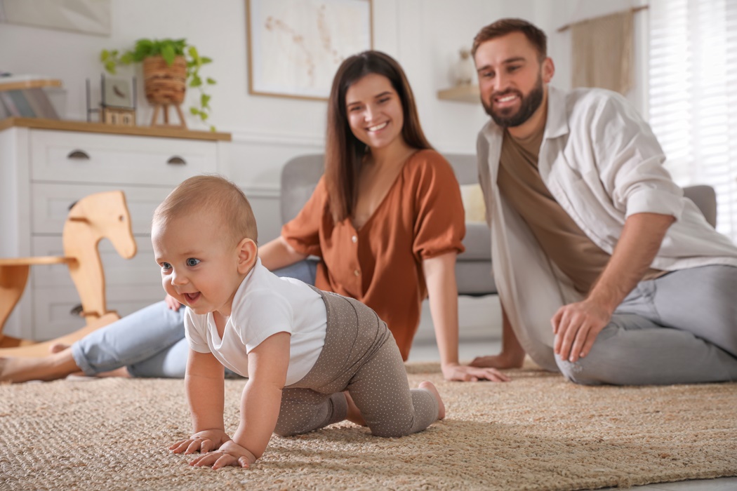 Happy parents watching their baby crawl on floor at home