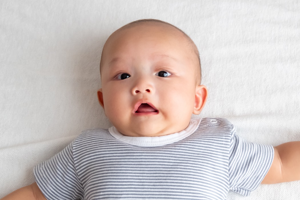A baby in a striped shirt lies shocked on the white carpet.