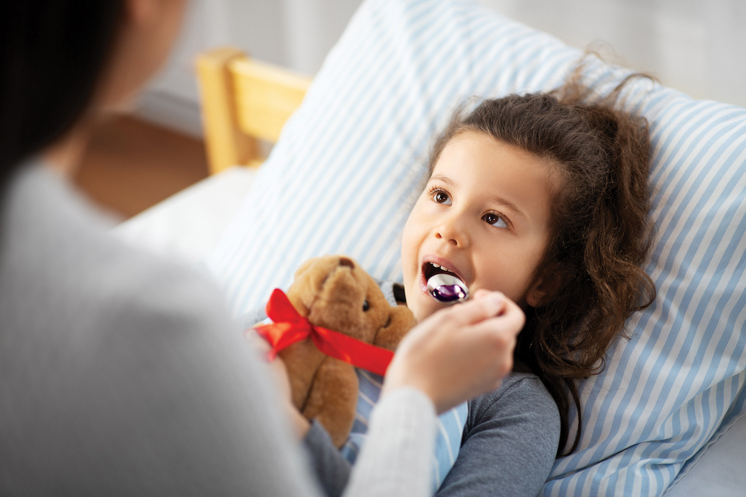 family, health and medicine concept - mother giving cough syrup to little sick daughter lying in bed at home