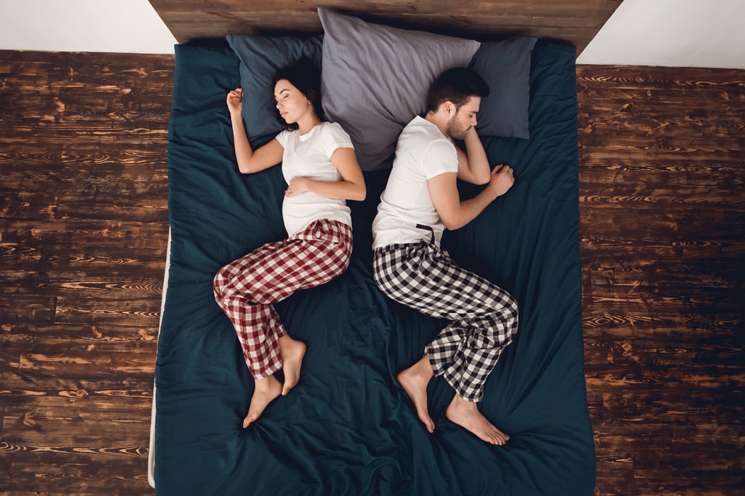 Top view. Young pregnant woman is sleeping back to back to man lying on big bed.