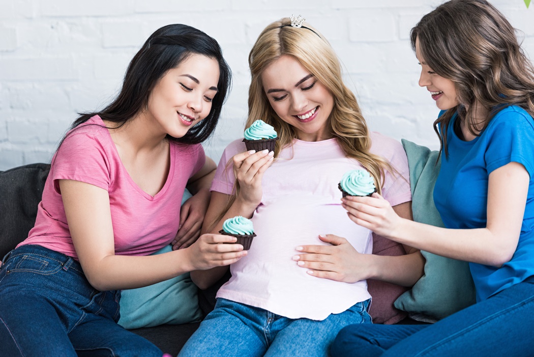 happy multicultural friends and pregnant woman with cupcakes at baby-party