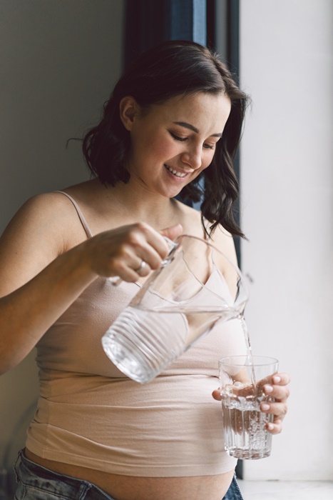 Pregnant woman drinking water near window. Pregnancy concept