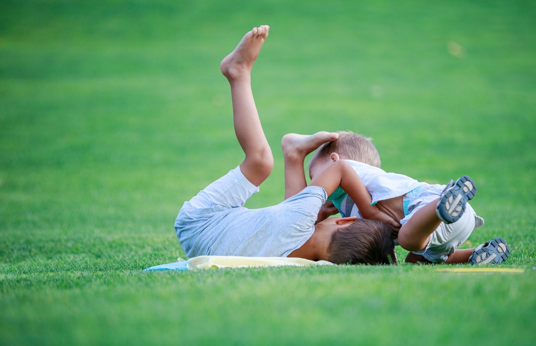 Two boys fighting outdoors. Siblings wrestling on grass in summe