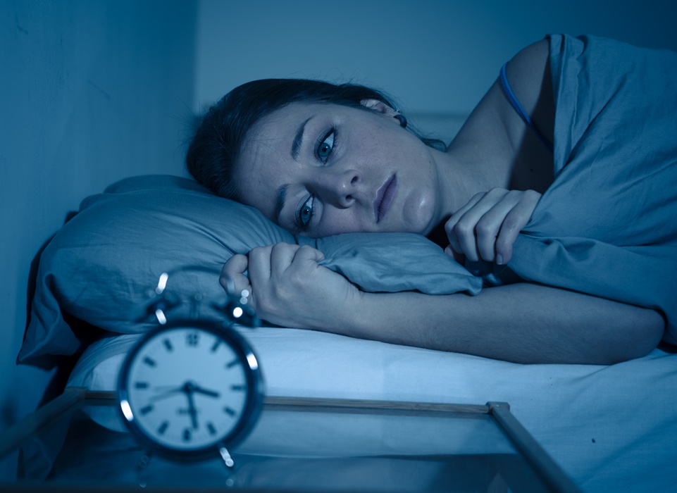 Attractive woman in bed staring at alarm clock trying to sleep feeling stressed and sleepless
