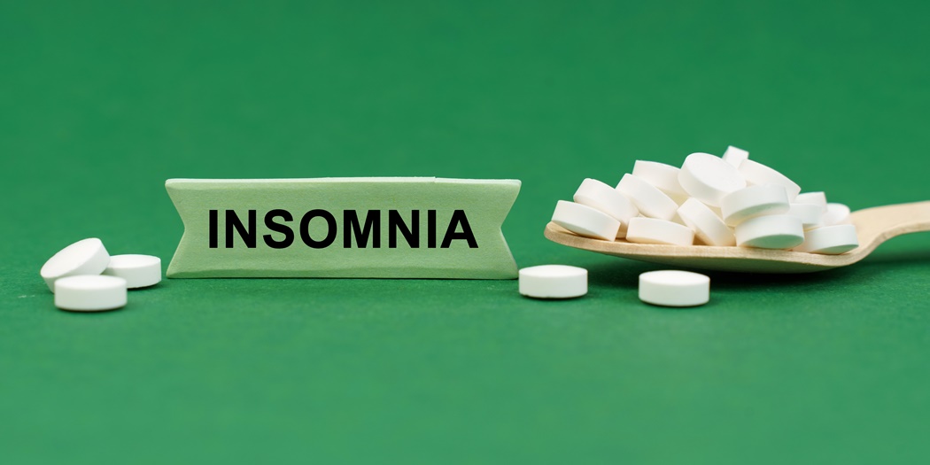 On a green surface, a wooden spoon with pills and a sign with the inscription - INSOMNIA