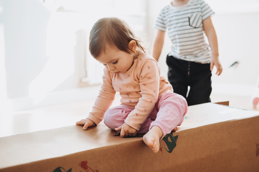 Close-up of a cute child standing on a large cardboard box containing a Christmas tree. New year holidays, artificial Christmas tree home decoration, biodegradable decor.