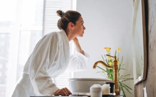 Young woman with dark long hair in white bathrobe near mirror in