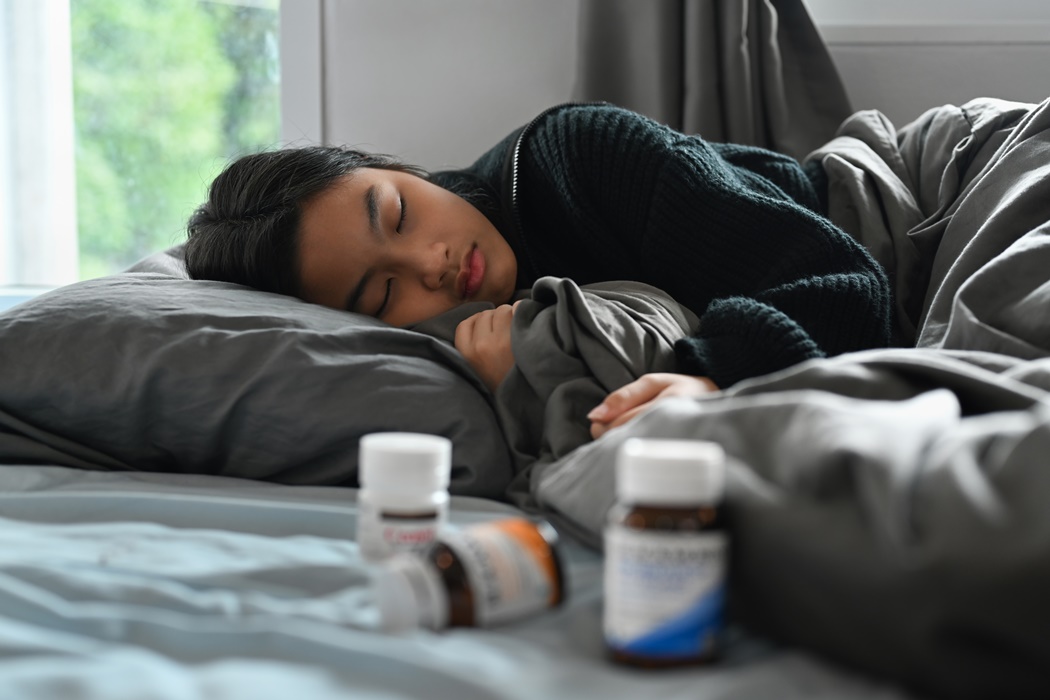 Sick little girl lying in bed under blanket with high fever and flu. Symptom of influenza, health problem concept