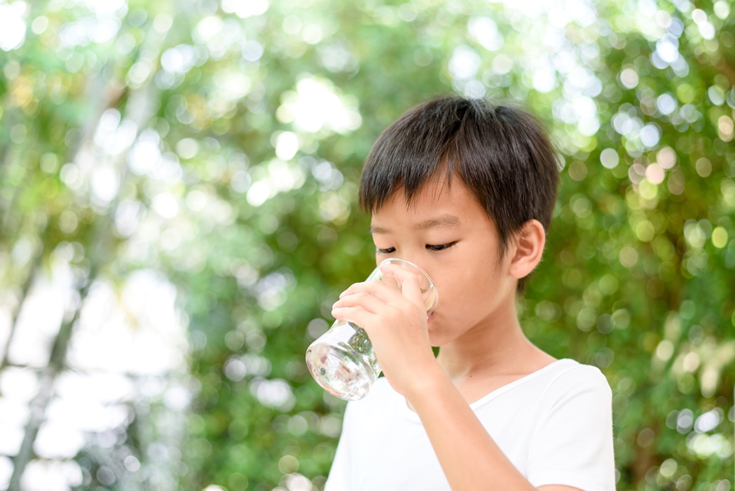 Young boy drink water from a glass.