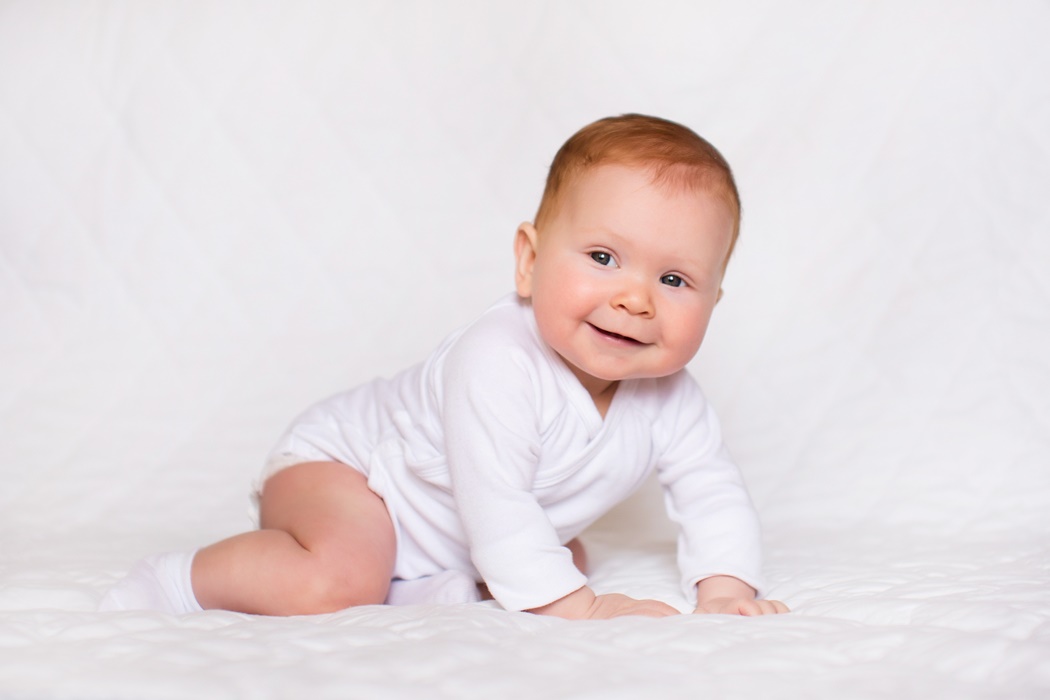 Little cute baby girl in white romper in bedroom.