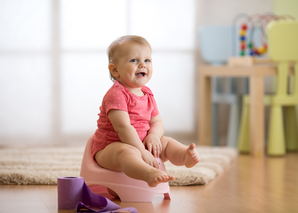 smiling baby sitting on chamber pot with toilet paper roll