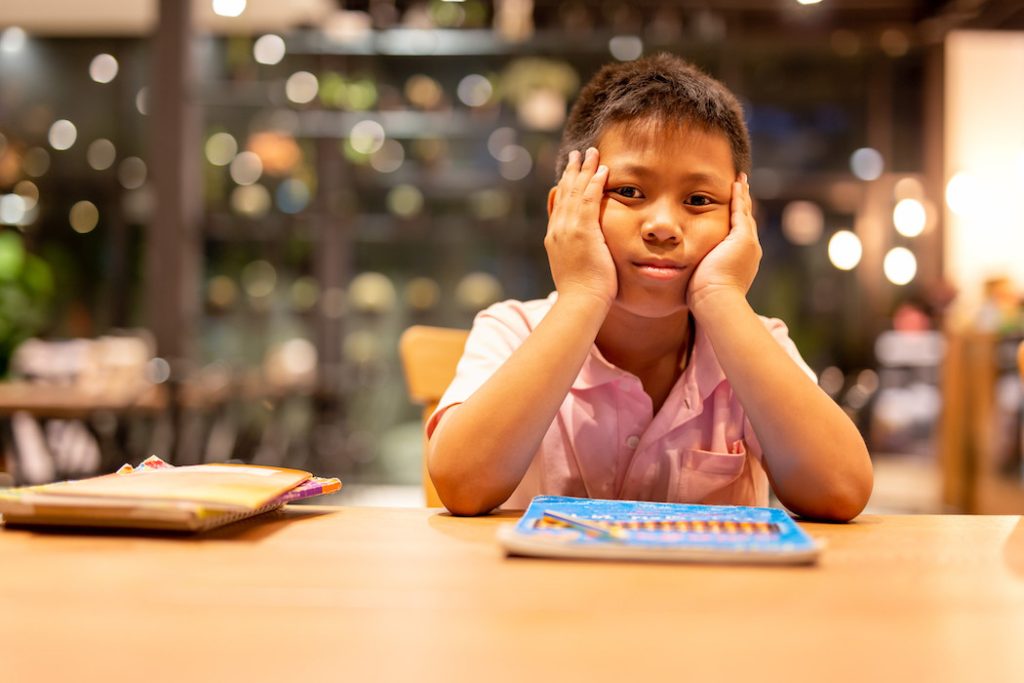 Asian school boy hand on his face dressed while doing his home work