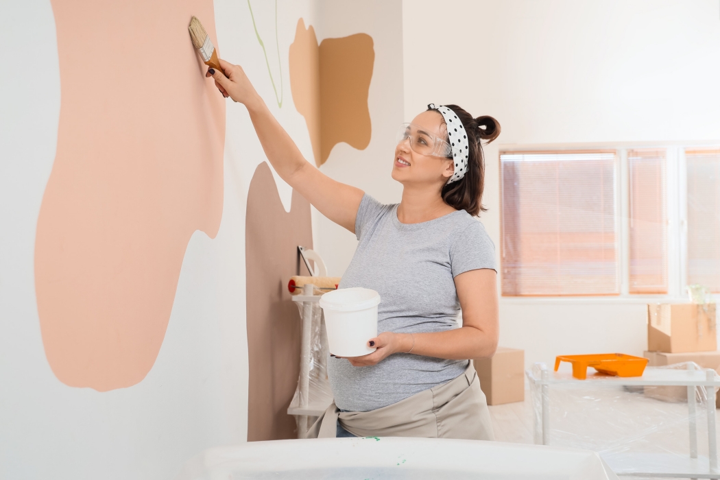 Young pregnant woman painting wall during repair in children's bedroom